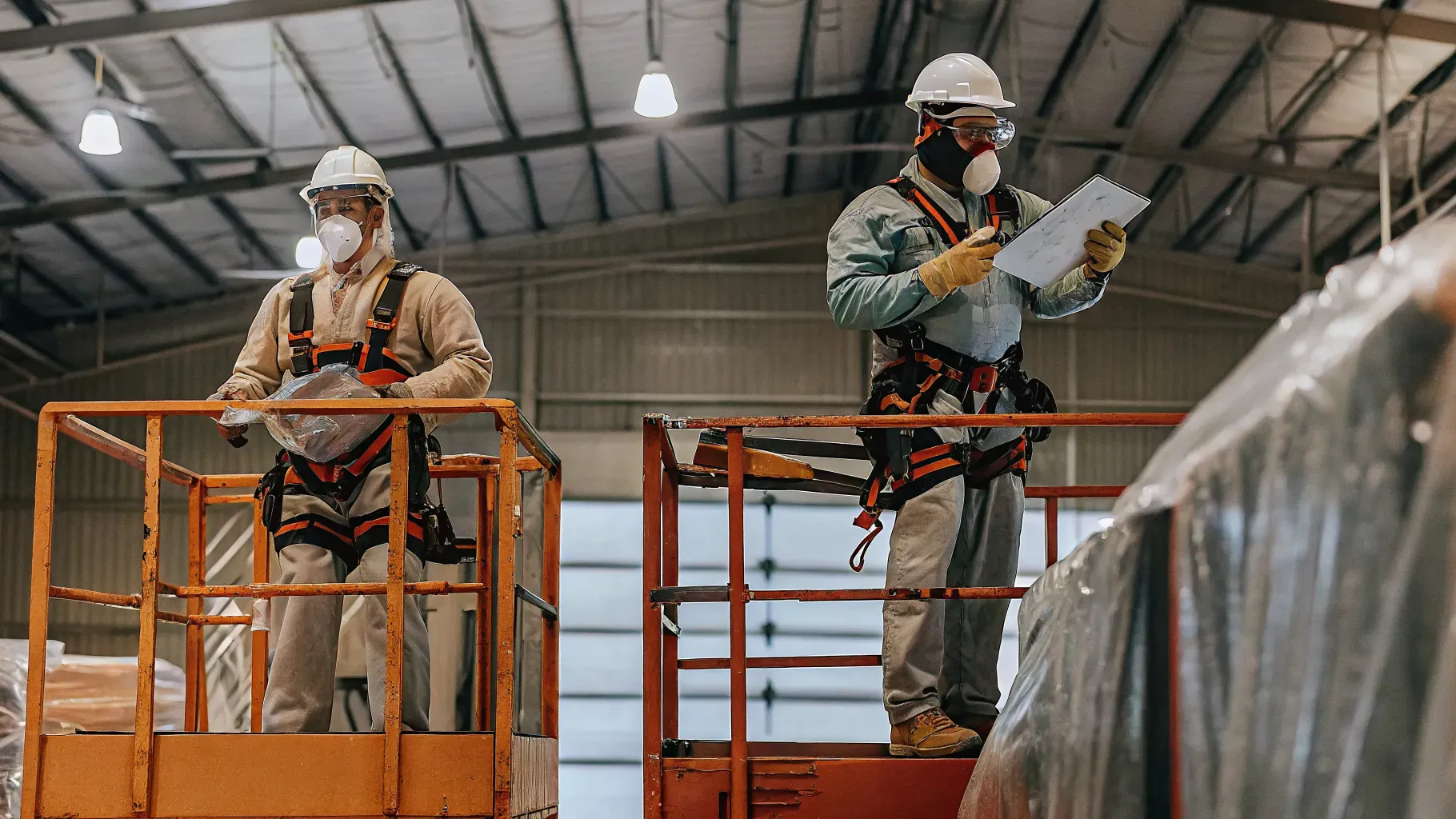 Painting crew in protective gear preparing a warehouse for painting with scissor lifts and protected inventory